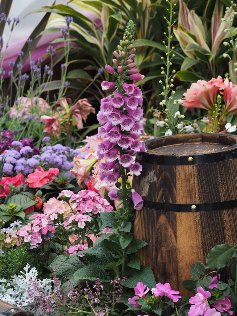 A colorful array of flowers surrounds a rustic wooden barrel, showcasing a lush garden landscape.